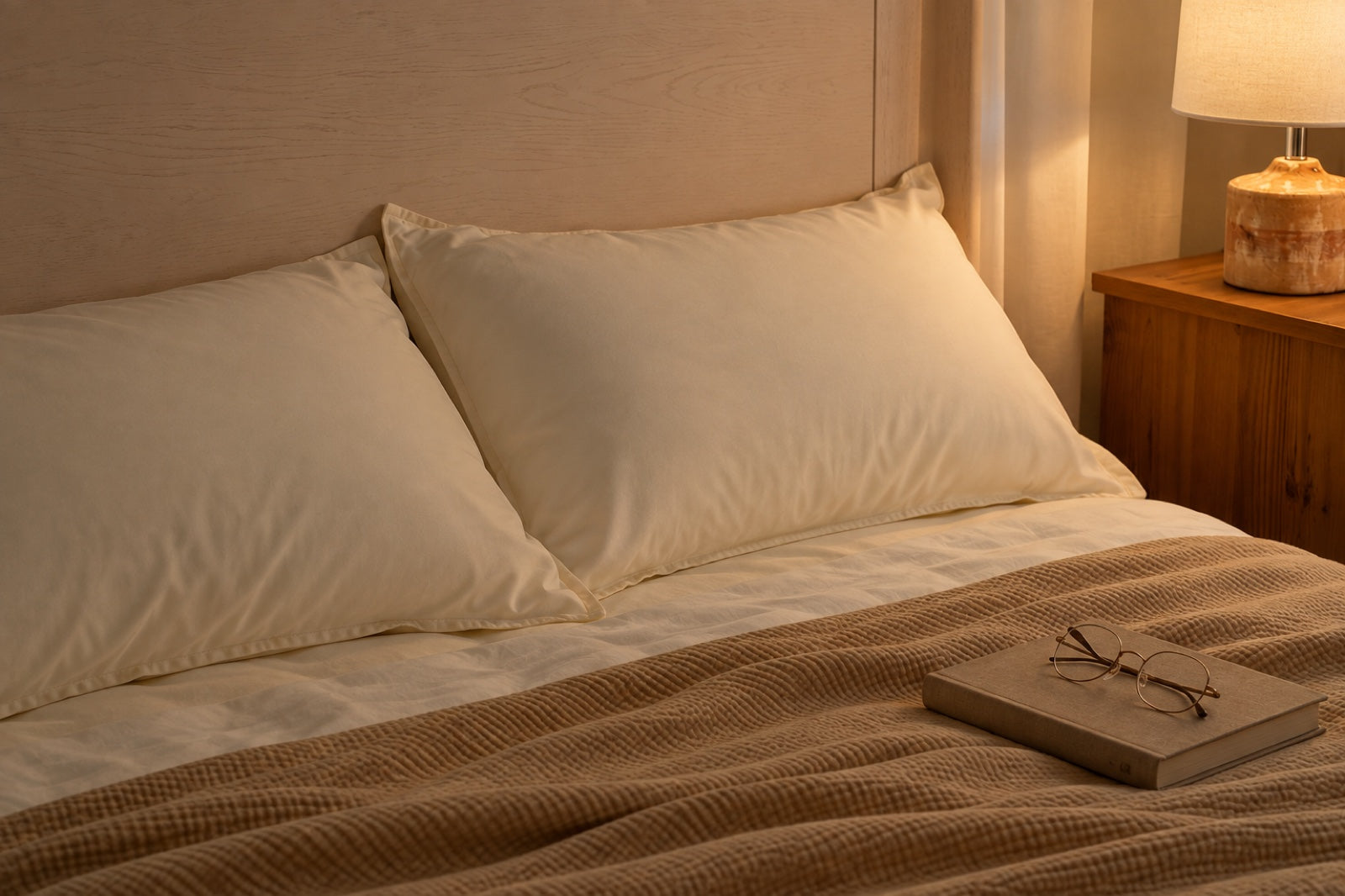 Pearl lyocell pillows with a book and reading glasses in warm bedside lamp light.